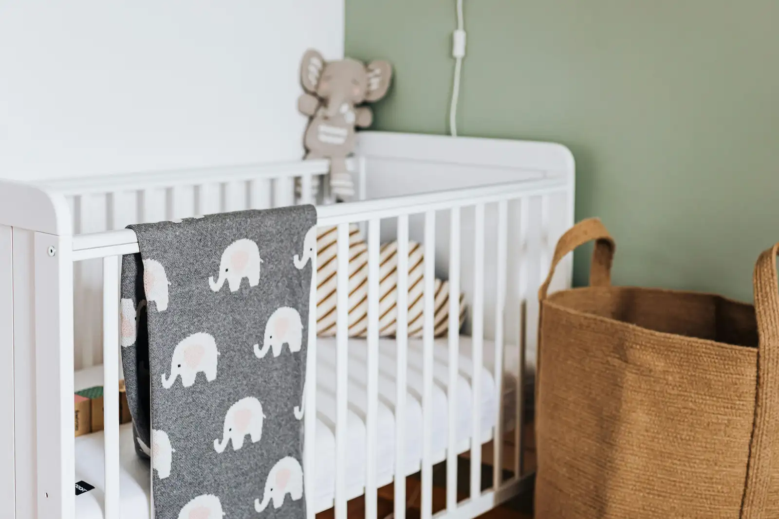 Cuna blanca con decoración de elefantes y toques verdes en dormitorio infantil.