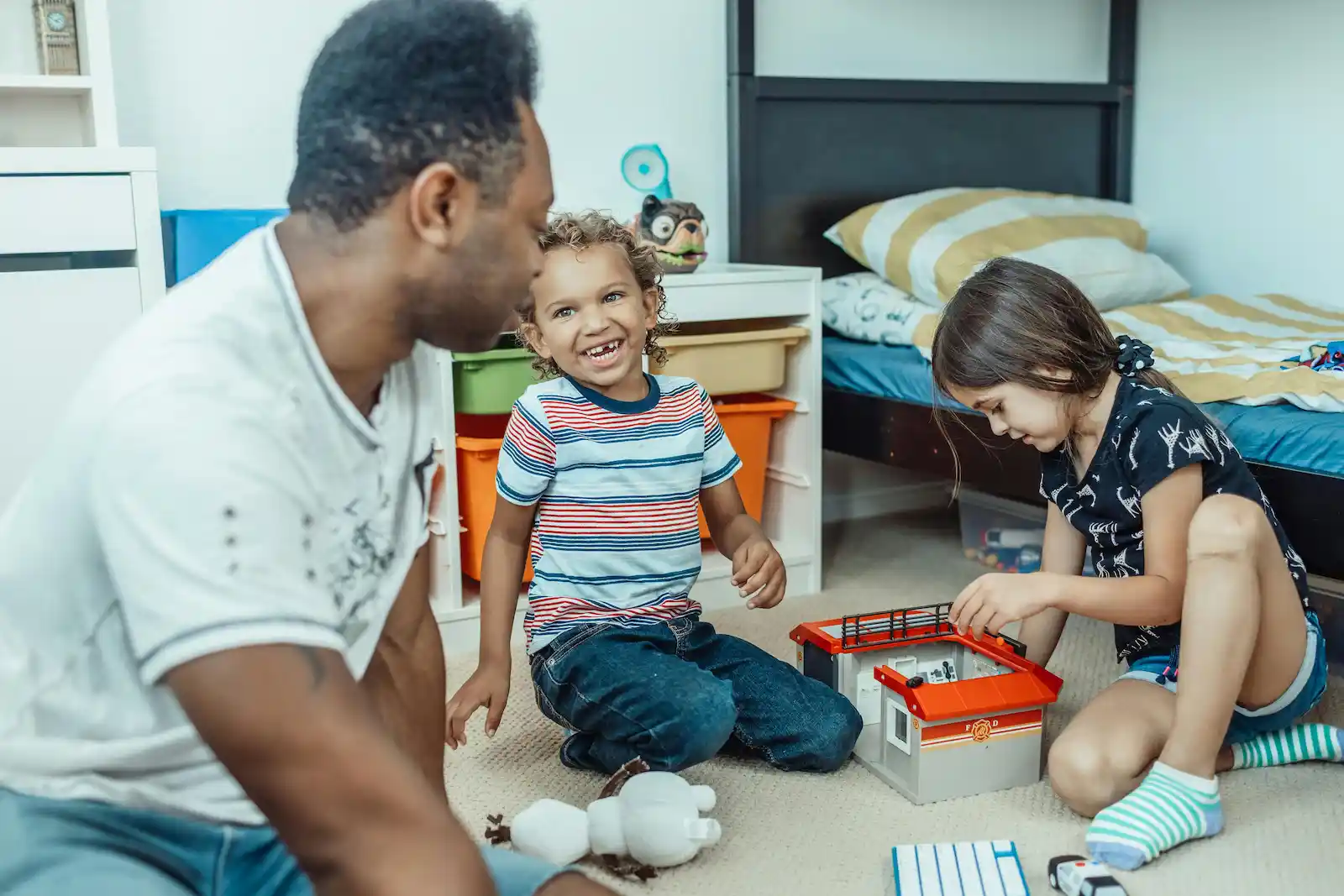 Papá jugando con su hija e hijo en un dormitorio bien iluminado.